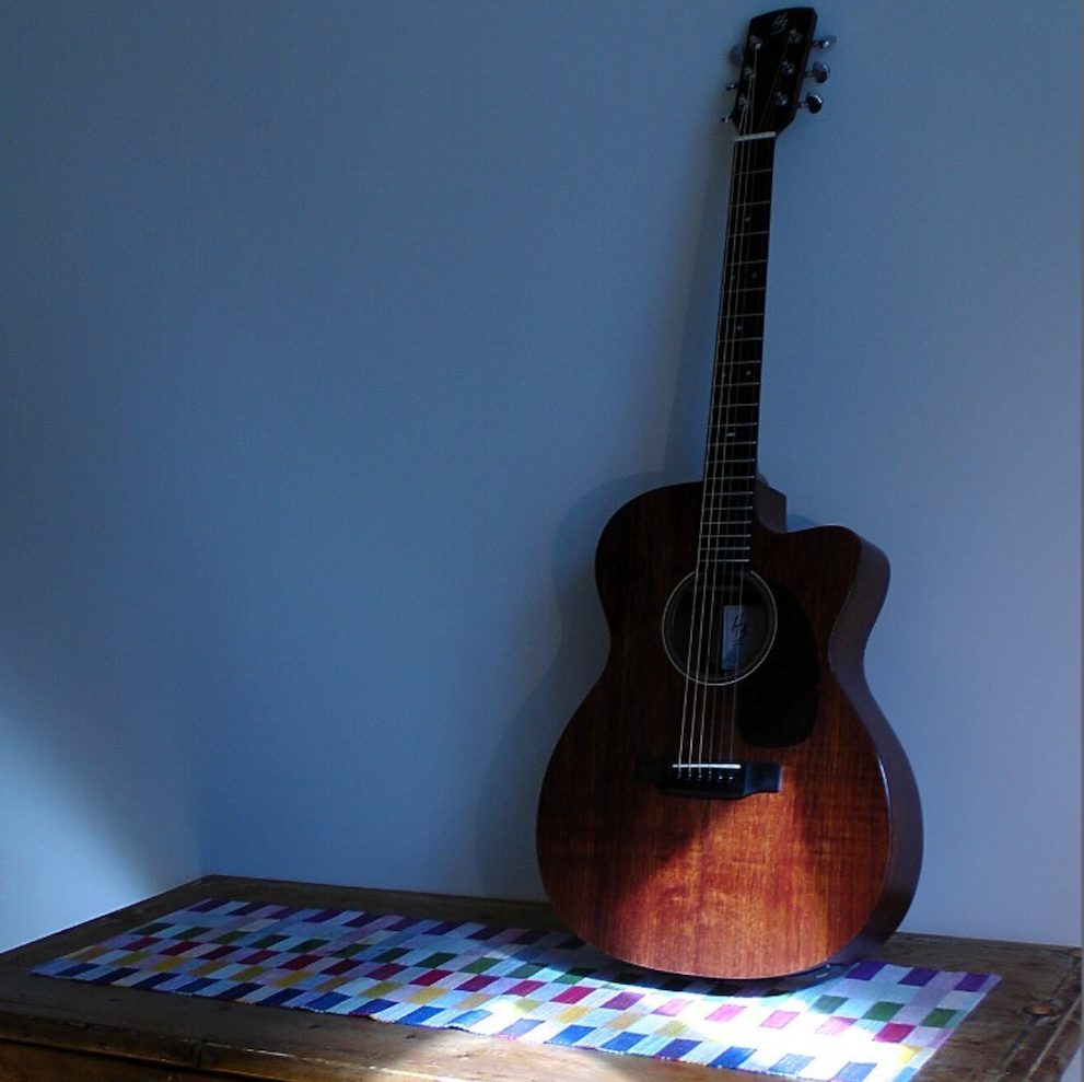 A guitar standing on an old table when sunlight comes in on part of the guitar.